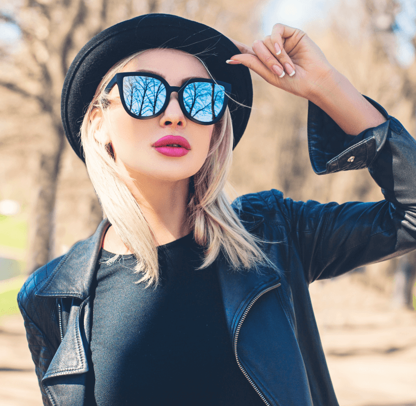 Modelka s blond vlasmi a čiernymi slnečnými okuliarmi, nosiaca čiernu koženú bundu a klobúk, vyžarujúca štýlovosť.